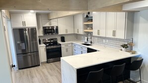 A modern kitchen with white cabinetry, stainless steel appliances, a marble countertop, and black bar stools. - *New 3BR/2BA* ~ 200 ft Lake Frontage ~ Lakehaven (Hot Springs)