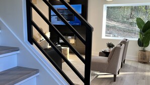 A staircase with wooden steps and black railings leading to a living area with a television, seating, and a large window. - *New 3BR/2BA* ~ 200 ft Lake Frontage ~ Lakehaven (Hot Springs)