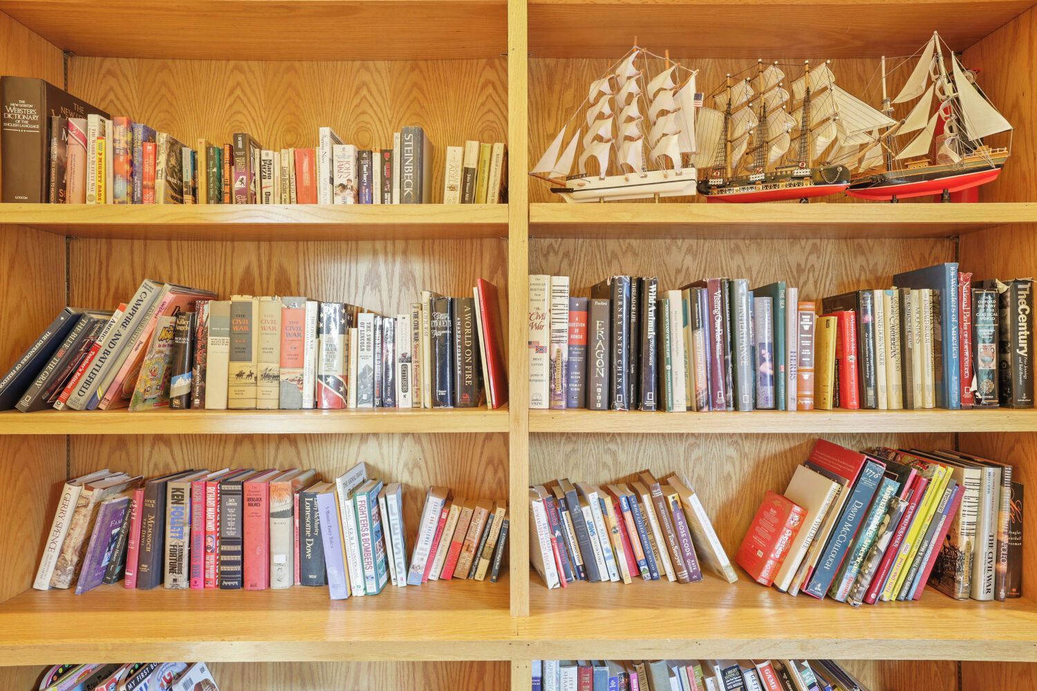 A bookshelf with various books and two model ships.