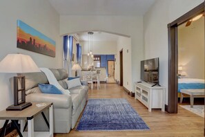 A modern living room with a sofa, a TV, a dining area, and a kitchen in the background.