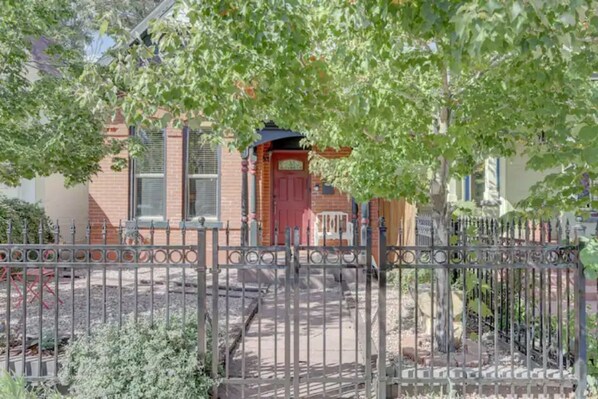 A gated residential area with a brick house, a red door, and a metal fence.