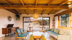 Un salon spacieux avec un plafond en bois, une grande fenêtre donnant sur le désert, un canapé, des fauteuils et une table basse.