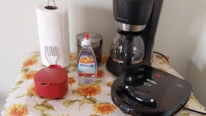 Una encimera de cocina con una cafetera, un recipiente rojo, una botella de agua y un rollo de toallas de papel.