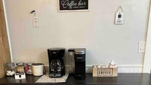 Eine Küchenarbeitsfläche mit Kaffeemaschine, Wasserkocher und einer Kaffeestation. Darunter befinden sich drei Barhocker.