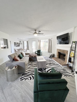 A modern living room with a sofa, armchairs, a coffee table, a fireplace, and a television.