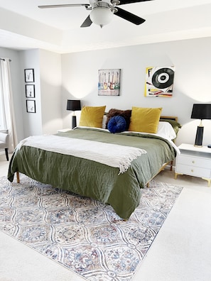 A bedroom with a bed, a ceiling fan, a nightstand, a lamp, and wall art.