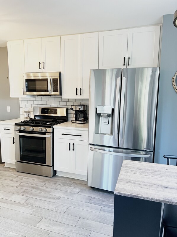 A modern kitchen with white cabinets, stainless steel appliances including a microwave, stove, oven, and refrigerator, and a coffee maker on the countertop.