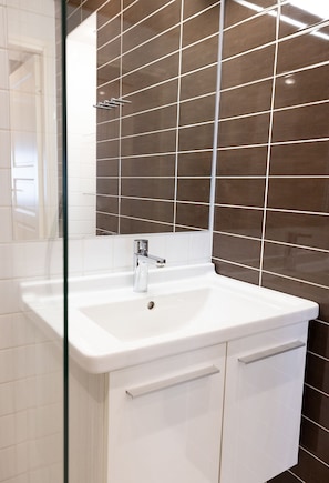 A bathroom with a white sink, chrome faucet, and a mirror. The walls are tiled in a dark brown pattern.