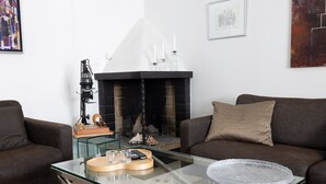 Uma sala de estar com uma mesa de centro de vidro, lareira, dois sofás e um tabuleiro de xadrez.