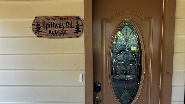 A brown wooden door with a glass panel, a welcome sign for Spillway Rd. Retreat, and a doormat with a paw print design.