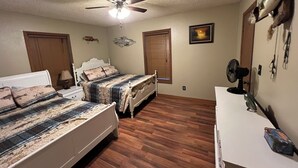 A bedroom with two beds, a ceiling fan, wooden flooring, a dresser, and wall decorations.