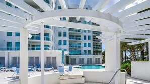 Un hôtel moderne doté d’une piscine, de chaises longues et d’un espace salon abrité.
