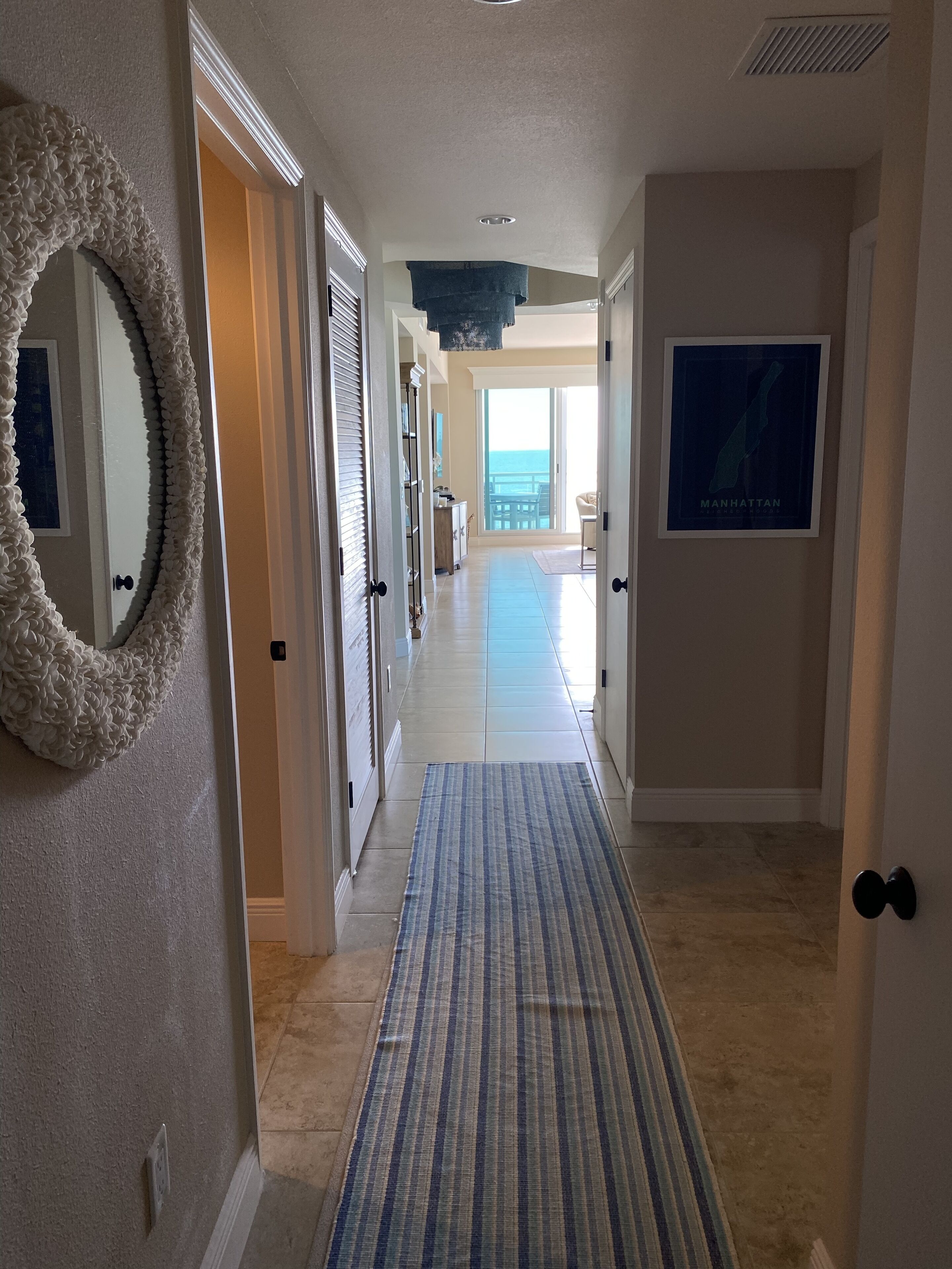 A hallway with a striped rug, a framed map, and a view of the ocean through large windows.