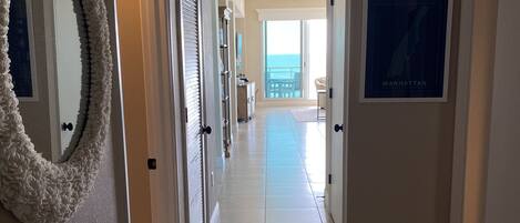 A hallway with a striped rug, a framed map, and a view of the ocean through large windows.