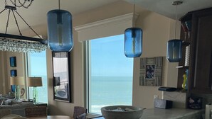 Une cuisine moderne dotée d’un grand îlot central, de luminaires suspendus et offrant une vue sur l’océan.