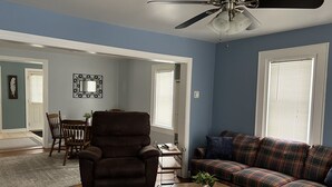 A living room with a brown leather chair, a plaid sofa, a wooden coffee table, and a ceiling fan. - Cozy Home located in downtown Big Bay (Big Bay)