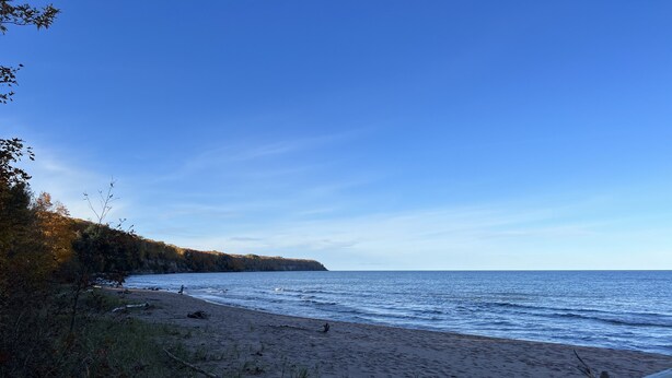 A beach with a wooden fence, sandy shore, and a cliff with trees. - Cozy Home located in downtown Big Bay (Big Bay)