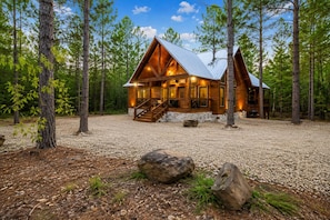 A log cabin with a stone foundation, wooden exterior, and a porch with steps leading to a deck.