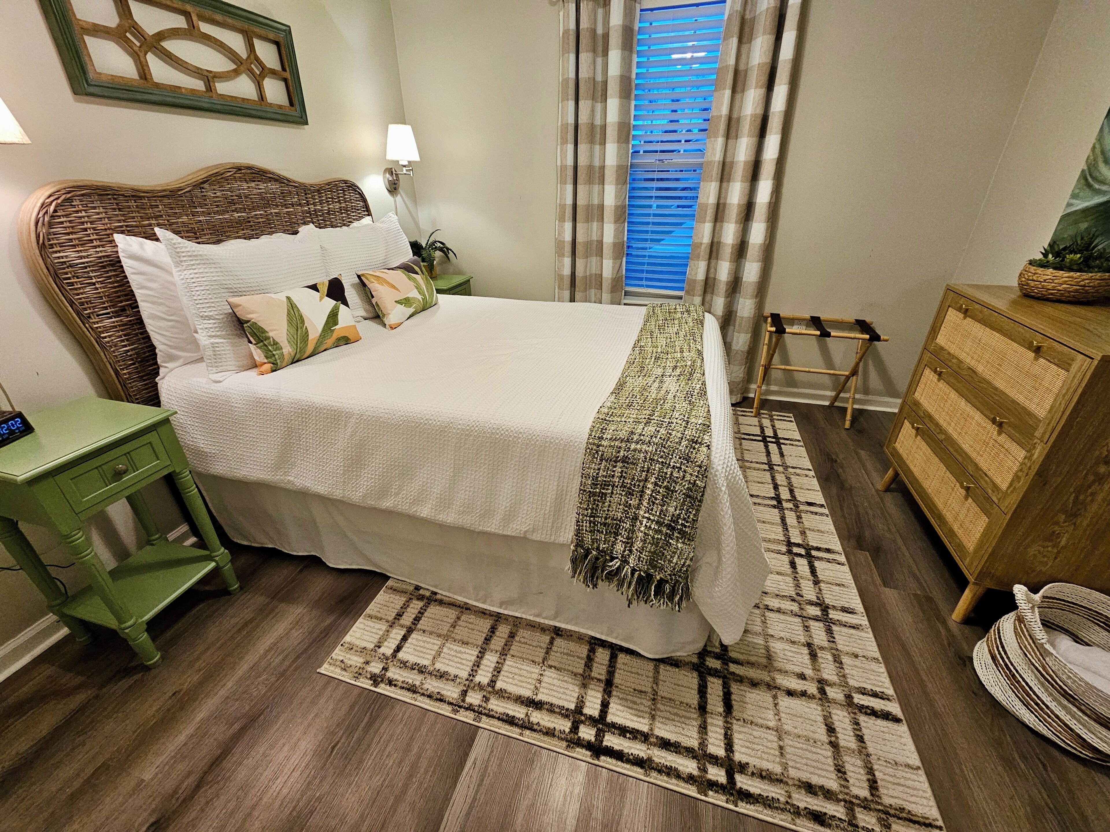 Un dormitorio ordenado con cama, mesitas de noche, cómoda y ventana con cortinas.