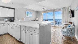 Una cocina moderna con armarios blancos, una isla grande y vistas al océano a través de un ventanal corredero.