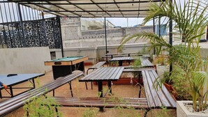 Un espacio de estar al aire libre con mesas y bancos de madera, rodeado de plantas en macetas.
