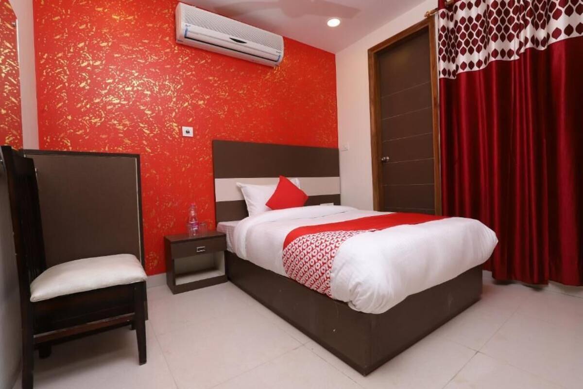 Une chambre d’hôtel avec un lit, une chaise, une table de chevet et une couvre-lit à motifs rouges et blancs.