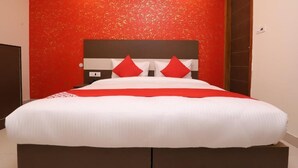Un grand lit avec une literie blanche et rouge, un mur rouge à texture et une tête de lit marron.