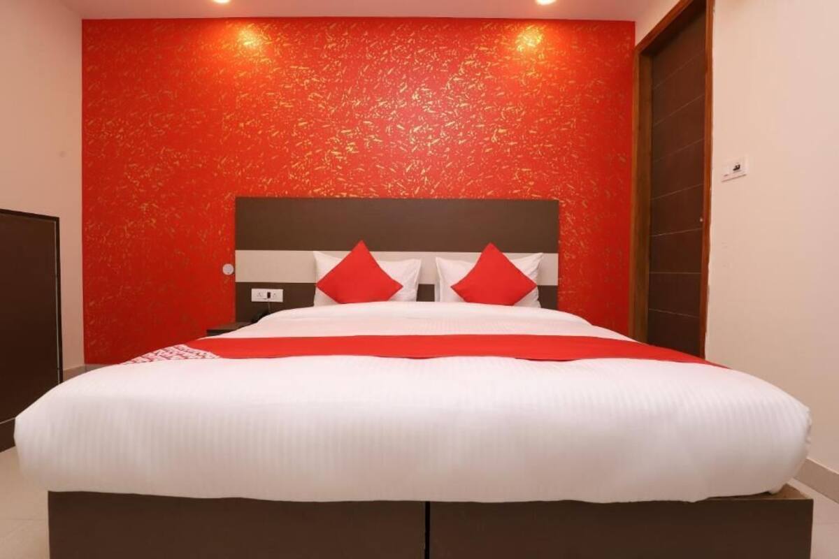 Un grand lit avec une literie blanche et rouge, un mur rouge à texture et une tête de lit marron.