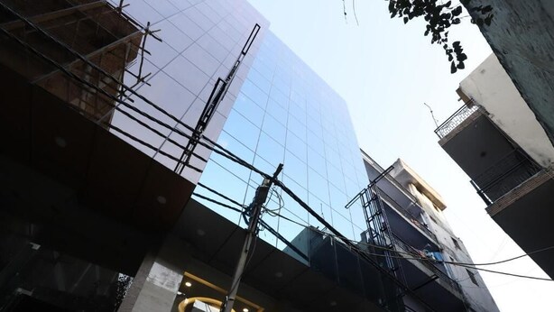 Un bâtiment moderne doté d’une façade en verre, d’un porche et d’échafaudages apparents.