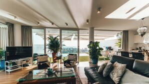 A modern living room with a large TV, comfortable seating, a glass coffee table, and a view of the city. - Villa Francia (Costa Adeje)