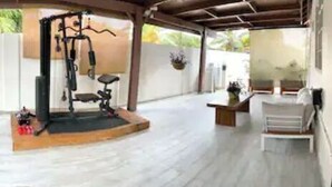 Een overdekte buitenruimte met een trainingsstation, zitplaatsen en potplanten.