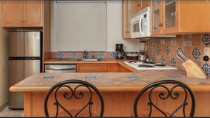 A kitchen with wooden cabinets, stainless steel appliances, a tiled backsplash, and a central island with chairs. - Beautiful Villa del Arco - Two Bedroom Suite (Cabo San Lucas)