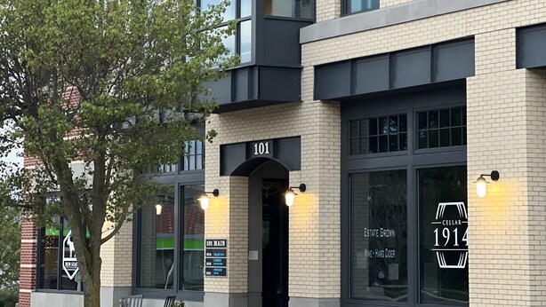 A modern building with a brick facade, numbered 101, featuring large windows and a well-maintained entrance area with a bench and potted plants. - Stay on Main, lovely 1 bedroom renovated unit (East Jordan)