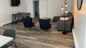 A modern living room with a dining area, a sofa, and a TV mounted on the wall. - Stay on Main, lovely 1 bedroom renovated unit (East Jordan)
