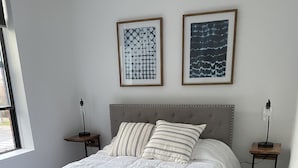 A bedroom with a bed, two bedside tables, a bench, and two framed pictures on the wall. - Stay on Main, lovely 1 bedroom renovated unit (East Jordan)