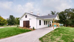 A white single-story house with a covered porch, a large barn door, and a small garden area. - The Chicken Coop on Highway H (Troy)