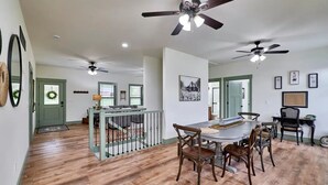 A spacious dining area with a wooden table and chairs, a staircase with a railing, and ceiling fans. - The Chicken Coop on Highway H (Troy)