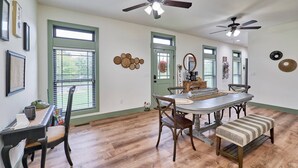 A dining area with a wooden table, chairs, and a bench. There are ceiling fans, windows with blinds, and wall decorations. - The Chicken Coop on Highway H (Troy)