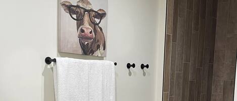 A bathroom with a wooden bench, a towel rack with two towels, and a cow-themed artwork on the wall.