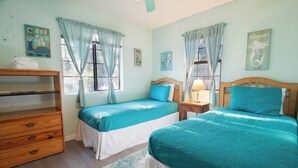 A room with two beds, a wooden dresser, and a window with curtains.