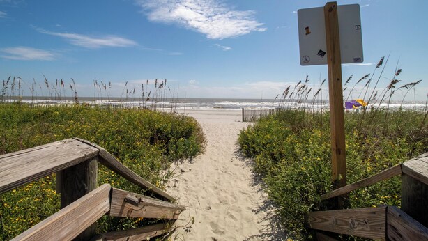 A wooden boardwalk leading to a beach with a signpost.