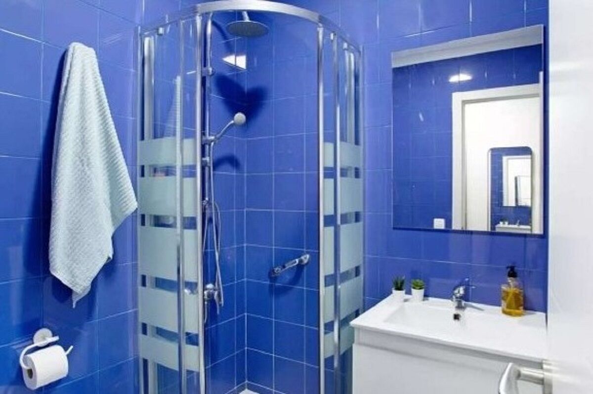 A bathroom with blue tiles, a glass shower enclosure, a white sink, and a mirror.