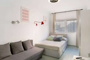 A modern room with a bed, a sofa, a red floor lamp, and a window with curtains.
