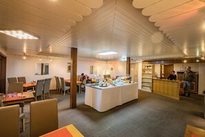 A spacious dining area with a central island, multiple tables, and chairs. There is a reception desk in the background. - Berghotel Waidmannsheil (Battenberg)
