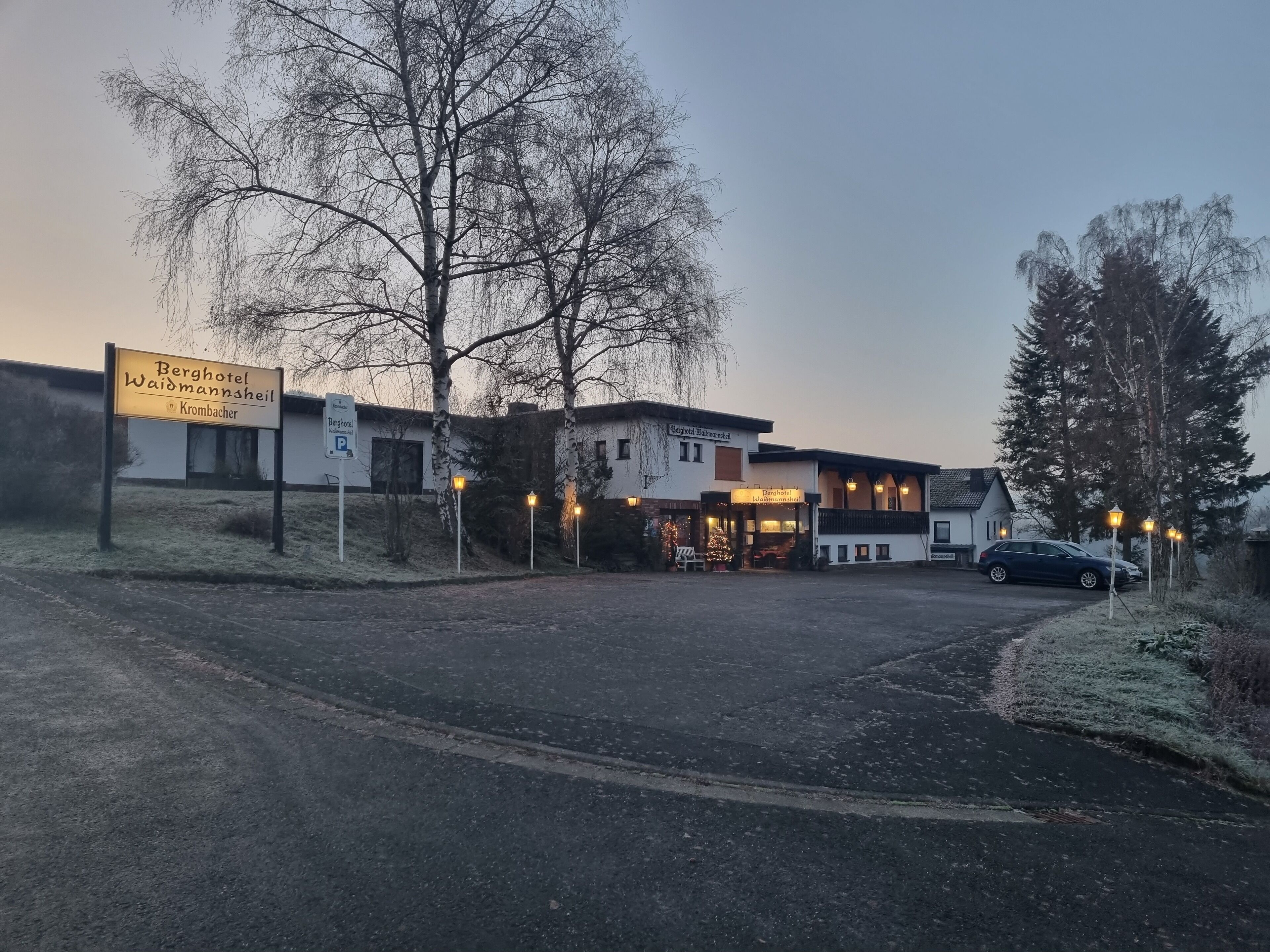 A hotel named 'Berghotel Waldmannsheil' with a parking sign, a covered outdoor seating area, and a car parked in front.