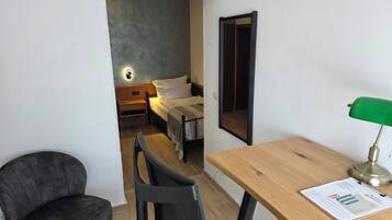 A small, modern room with a bed, a desk, a chair, and a mirror.