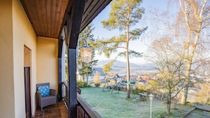 A covered porch with a wicker chair and a lantern, overlooking a grassy yard with a swing set and trees.