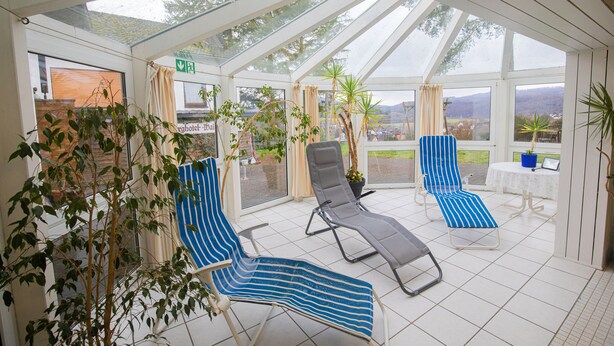A covered outdoor area with three lounge chairs, a table, and potted plants.