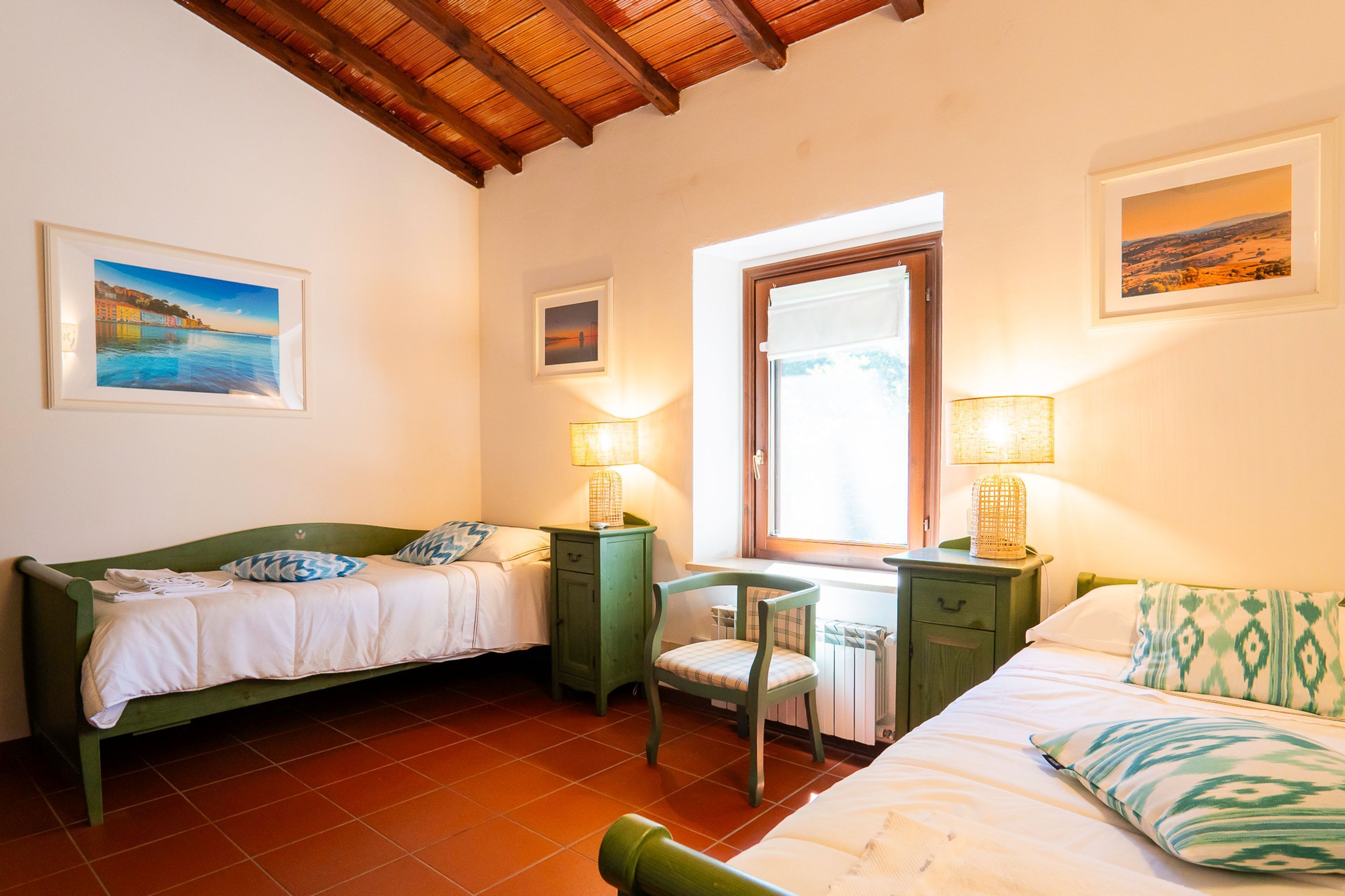 A bedroom with two beds, a desk, and a chair. There are two bedside tables with lamps.