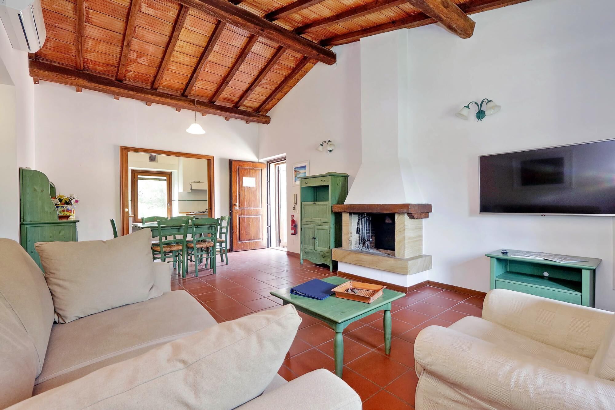 A living room with a fireplace, green furniture, a television, and a dining area with chairs and a table.